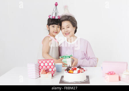 Petite-fille et sa grand-mère en mettant la tête sur l'autre et la tenue d'une boîte cadeau ensemble les deux en regardant party hat Banque D'Images