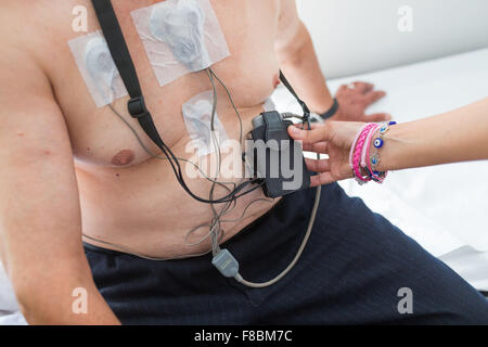 Placez les électrodes sur la poitrine d'un patient de sexe masculin, connecté à un moniteur Holter à sa taille. Un moniteur Holter est un électrocardiographe portable (ECG). Il peut mesurer et enregistrer l'activité électrique du cœur du patient dans les 24 heures, et détecter Banque D'Images