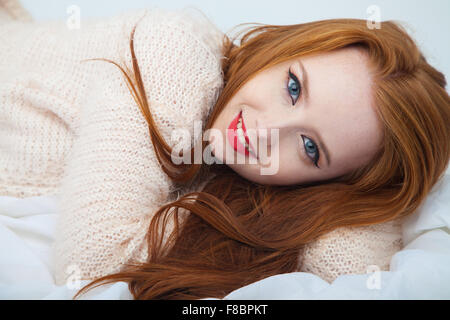 Une jolie femme rousse allongée sur tissu blanc. Banque D'Images