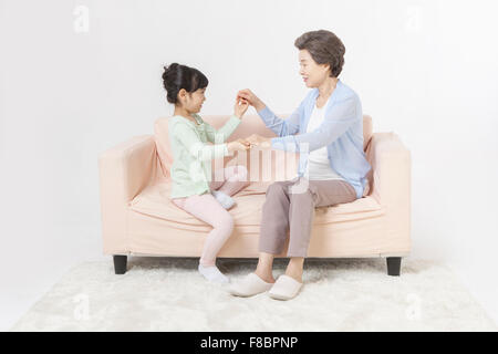 Grand-mère et petite-fille tenant la main et en s'amusant les deux assis sur un canapé et regarder Banque D'Images