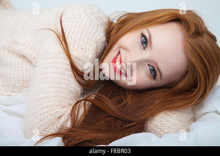 Un heureux à la femme aux cheveux rouge couché sur tissu blanc. Banque D'Images