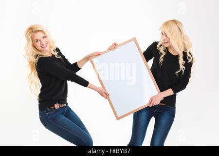 Deux ravissantes sœurs jumelles blondes s'amusant holding blank board over white background Banque D'Images