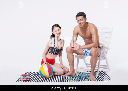 Femme à genoux sur une serviette avec un ballon de plage et d'un homme assis sur une chaise en regardant nager portent en avant avec un sourire Banque D'Images