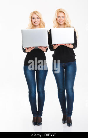 Deux jeunes soeurs jumelles blonde avec des ordinateurs portables sur fond blanc Banque D'Images