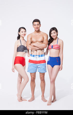 L'homme musclé en natation short debout entre deux femmes en bikini style rétro regarder tous de l'avant avec un sourire Banque D'Images