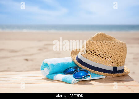 Chapeau, lunettes de soleil sur le matériau bois serviette non mise au point avec l'arrière-plan de plage Banque D'Images