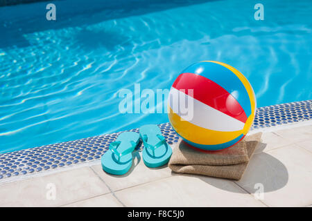 Les tongs, ballon de plage, serviette et placés sur du carrelage avec le fond de la piscine Banque D'Images