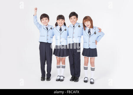 Quatre enfants d'âge scolaire élémentaire se tenant ensemble avec leurs bras autour de l'autre et souriant Banque D'Images