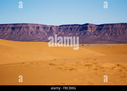 Dune de sable près de Ouarzazate avec montagnes en arrière-plan sous un soleil éclatant et un ciel bleu Banque D'Images