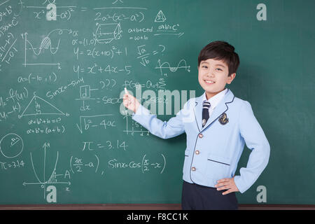 L'âge de l'école élémentaire boy in school uniforms écrit avec une craie sur un tableau noir avec formule mathématique et écrit Banque D'Images