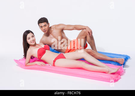 Woman in red bikini allongé sur un flotteur et un homme en pantalon natation couché à côté d'elle avec un genou soulevé les deux yeux de l'avant Banque D'Images