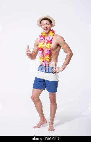 L'homme musclé en natation, pantalon, chapeau debout portant un collier de fleurs avec ses pouces vers le haut avec un sourire Banque D'Images