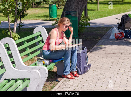 La jeune fille attire l'assis sur un banc dans un parc de la ville Banque D'Images