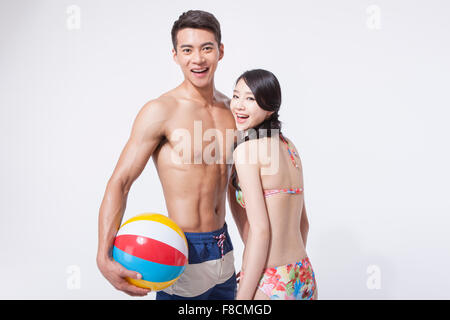 Couple dans les vêtements de plage ensemble regardant de l'avant avec un sourire et l'homme tenant un ballon de plage Banque D'Images