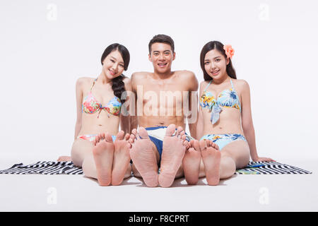 En natation homme pantalon entre deux femmes en bikini tous assis sur une serviette avec un sourire Banque D'Images