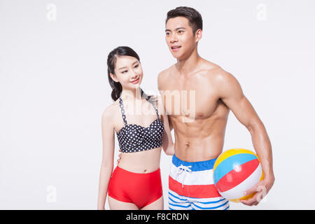 Couple dans les vêtements de plage avec leurs bras autour de l'autre et l'homme tenant un ballon de plage Banque D'Images