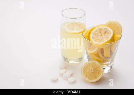 Verre de limonade avec une tranche de citron et des tranches de citron dans un autre verre et en vitamine comprimés placés avec eux Banque D'Images