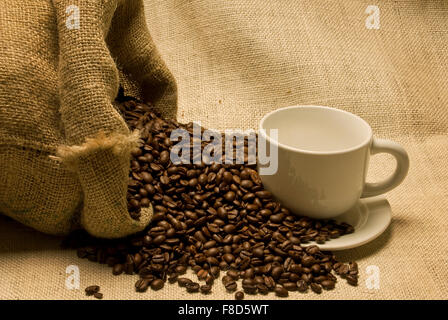 Tasse et soucoupe d verser les grains de café à partir de sac de toile sur un fond de toile Banque D'Images