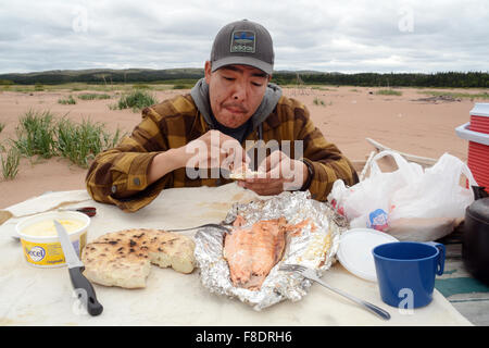 Un homme de la Première Nation Innue de creuse dans certains saumons et du bannock dans la ville de Pakua Shipi, Basse-Côte-Nord, Québec, Canada. Banque D'Images