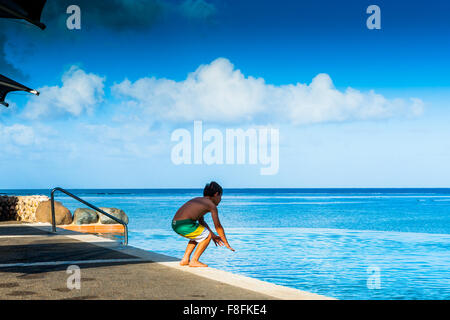 Un jeune garçon commence à plonger dans une superbe piscine à débordement sur l'île tropicale de Fidji dans le Pacifique sud. Banque D'Images