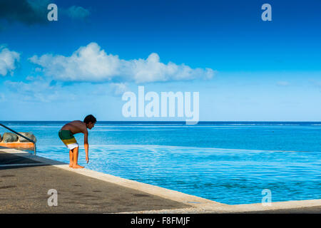 Un jeune garçon teste l'eau dans une superbe piscine à débordement sur l'île tropicale de Fidji dans le Pacifique sud. Banque D'Images