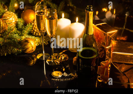 Arrangement de fête romantique blanc avec des bougies allumées, décoré des branches de pins, coffrets cadeaux enveloppés dans du papier brillant doré, flûte à champagne et verres pour célébrer Noël ou Nouvel An. Banque D'Images