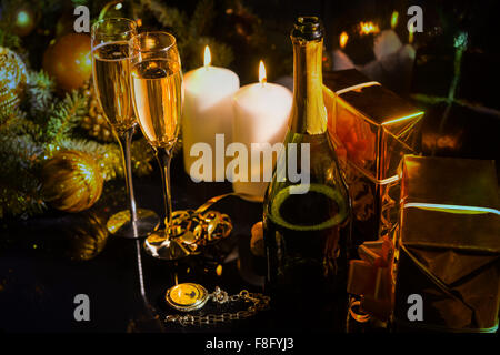 Arrangement de fête pour célébrer la nouvelle année, avec des bougies, champagne, des branches de pins, boules de Noël et les coffrets cadeaux enveloppés dans du papier brillant or. Banque D'Images