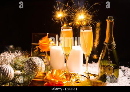 La vie encore de fête de célébration - verres de champagne avec brûler des cierges merveilleux sur la surface couverte de neige avec des bougies allumées, les cadeaux emballés d'or et les décorations de Noël en face de l'arrière-plan noir. Banque D'Images