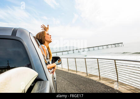 Caucasian woman leaning out car window at beach Banque D'Images