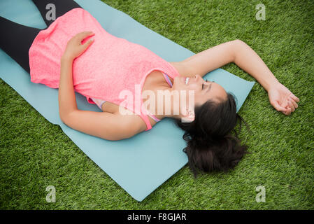 Chinese woman laying in grass on yoga mat Banque D'Images