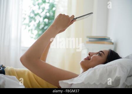 Hispanic woman using digital tablet in bed Banque D'Images