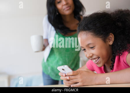 Mère regardant fille utiliser cell phone Banque D'Images