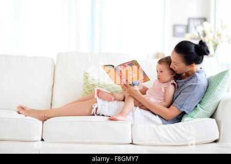 Mère et fille bébé lecture sur canapé Banque D'Images