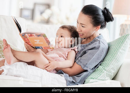 Mère et fille bébé lecture sur canapé Banque D'Images