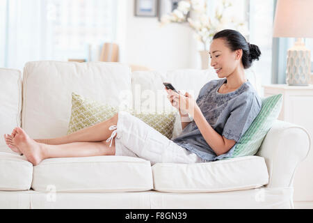 Japanese woman using cell phone on sofa Banque D'Images