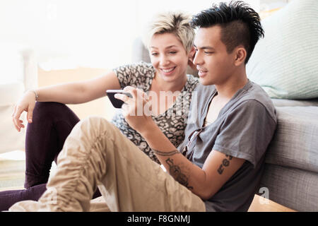 Couple using cell phone in living room Banque D'Images