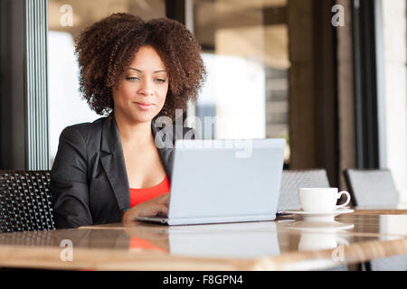 Mixed Race businesswoman using laptop in cafe Banque D'Images