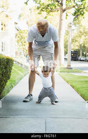 Père aider bébé à pied sur un trottoir