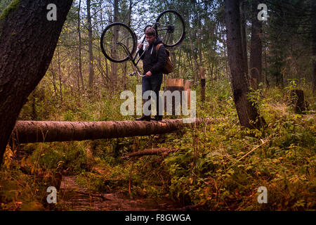 Caucasian man carrying bicycle on fallen tree Banque D'Images