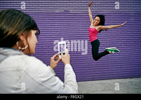 Woman photographing ami sauter de joie Banque D'Images