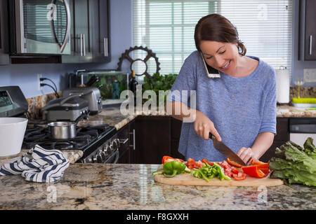 Mixed Race Woman talking on phone et hacher les légumes Banque D'Images