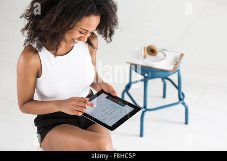 Une jeune femme afro-américaine à l'aide d'un comprimé ou de l'iPad dans un paramètre de type studio Banque D'Images