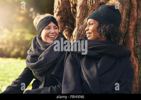 Close-up of two young women leaning on tree trunk dans le parc d'automne et à l'un l'autre Banque D'Images