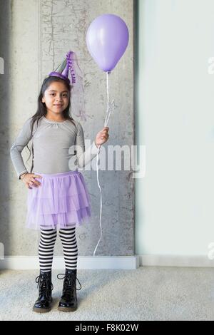 Portrait of young girl wearing party, vêtements, holding purple balloon Banque D'Images