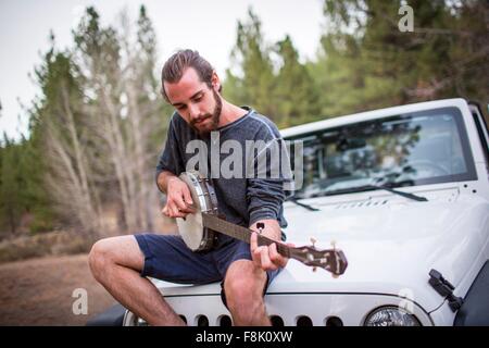 Jeune homme jouant du banjo sur capot jeep, Lake Tahoe, Nevada, USA Banque D'Images
