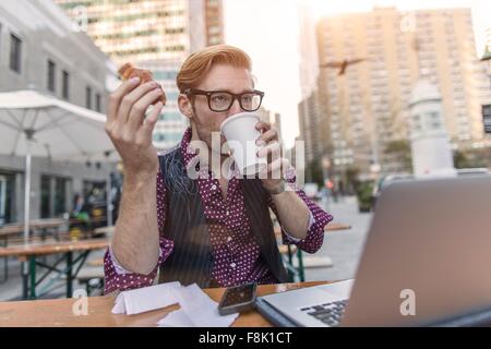 Jeune homme a souligné se dépêchant déjeuner de travail at sidewalk cafe, New York, USA Banque D'Images