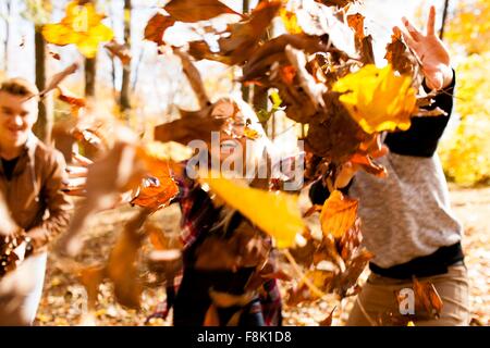 Jeune femme et deux jeunes frères de jeter les feuilles d'automne en forêt Banque D'Images