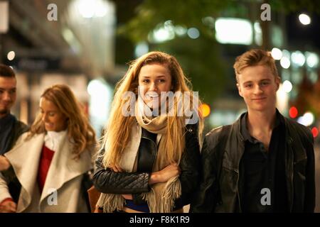 Deux jeunes couples se promener bras dessus bras dessous le long de rue la nuit, Londres, UK Banque D'Images