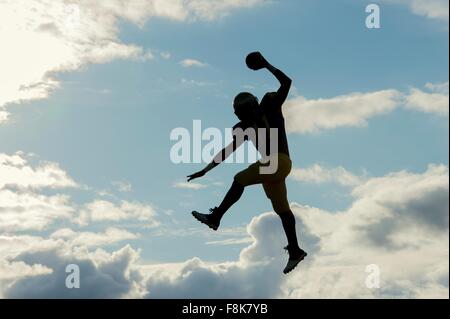 Teenage american football player, sautant avec balle, mid air Banque D'Images