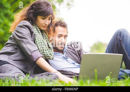 Jeune couple assis sur l'herbe à la recherche vers le bas à l'aide de l'ordinateur portable Banque D'Images